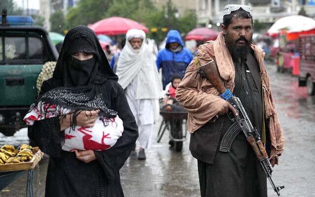 An Afghan woman walks through the old market as a Taliban fighter stands guard, in downtown Kabul, Afghanistan, May 3, 2022. (AP Photo/Ebrahim Noroozi)