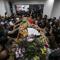 Palestinians surround the Palestinian flag-draped body of veteran Al Jazeera journalist Shireen Abu Akleh, as it is brought to the news channel's office in the West Bank city of Ramallah, on May 11, 2022. (Abbas Momani/Pool via AP)