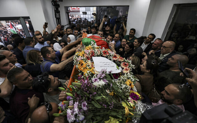 Palestinians surround the Palestinian flag-draped body of veteran Al Jazeera journalist Shireen Abu Akleh, as it is brought to the news channel's office in the West Bank city of Ramallah, on May 11, 2022. (Abbas Momani/Pool via AP)