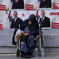 A homeless woman sits in front of campaign posters for a candidate in the upcoming parliamentary elections in Beirut, Lebanon, May 9, 2022. (AP Photo/Hassan Ammar)