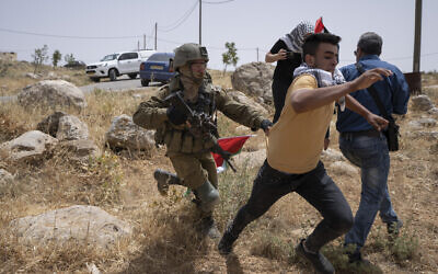 An Israeli soldier chases a protester while Palestinian, Israeli and foreign peace activists attempt to open a road that passes close to the Israeli outpost of Mitzpe Yair to Masafer Yatta in the West Bank on May 13, 2022. (AP Photo/Nasser Nasser)