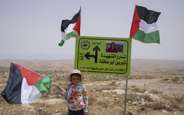 A girl carry a Palestinian flag in front of a directions sign with a picture of slain Al Jazeera journalist Shireen Abu Akleh while Palestinian, Israeli and foreign peace activists protest against evictions in Masafer Yatta in the West Bank on May 13, 2022. (AP Photo/Nasser Nasser)