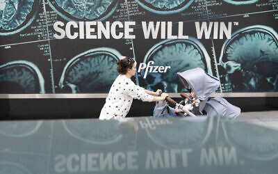 A woman pushes a baby in a stroller past a sign hanging outside Pfizer headquarters in New York, May 23, 2022. (Mary Altaffer/AP)