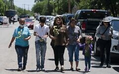 People walk with flowers to honor the victims in Tuesday's shooting at Robb Elementary School in Uvalde, Texas, Wednesday, May 25, 2022 (AP Photo/Jae C. Hong)