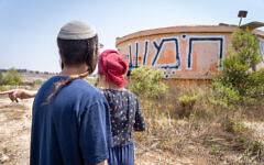 Visitors walk by the water tower on the ruins of the evacuated settlement of Homesh on August 27, 2019. (Hillel Maeir/Flash90)