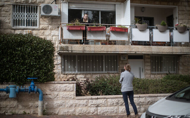 A woman talks to a friend from her apartment balcony, during the COVID-19 pandemic in Jerusalem on March 31, 2020. (Hadas Parush/Flash90)