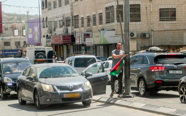 A Israeli man removes a Palestinian flag from a lamppost in the West Bank town of Hawara, near Nablus, May 22, 2022.(Nasser Ishtayeh/Flash90)