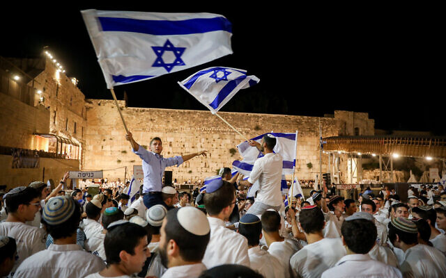 Jewish men dance with Israeli flags at the Western Wall in Jerusalem Old City on the eve of Jerusalem Day, May 28, 2022. (Noam Revkin Fenton/Flash90)