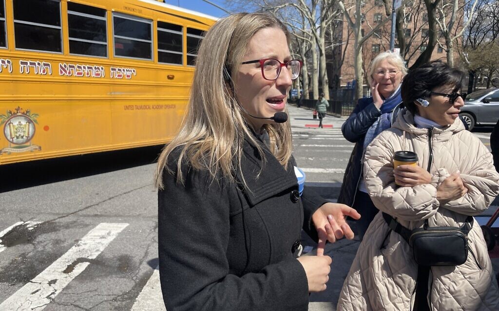 Frieda Vizel speaks to participants of her tour of Williamsburg, New York, in front of a school bus with Yiddish lettering, April 2022. (Danielle Ziri)