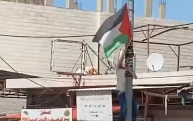 An Israeli removes a Palestinian flag from a pole in the Palestinian town of Hawara on May 20, 2022. (Screen capture/Twitter)