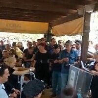Mourners listen to the wife of former Meretz MK Ilan Gilon at the social activist's funeral in Kfar Saba, May 3, 2022 (Screen grab)
