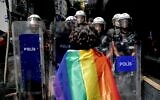 A participant faces riot policemen wearing a rainbow flag during a Pride march in Istanbul, on June 26, 2022. (KEMAL ASLAN / AFP)