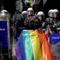 A participant faces riot policemen wearing a rainbow flag during a Pride march in Istanbul, on June 26, 2022. (KEMAL ASLAN / AFP)