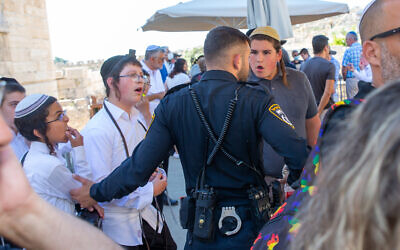A police officer stands between a group of ultra-Orthodox youths and a bar mitzvah ceremony at the egalitarian section of the Western Wall on June 30, 2022. (Laura Ben-David)