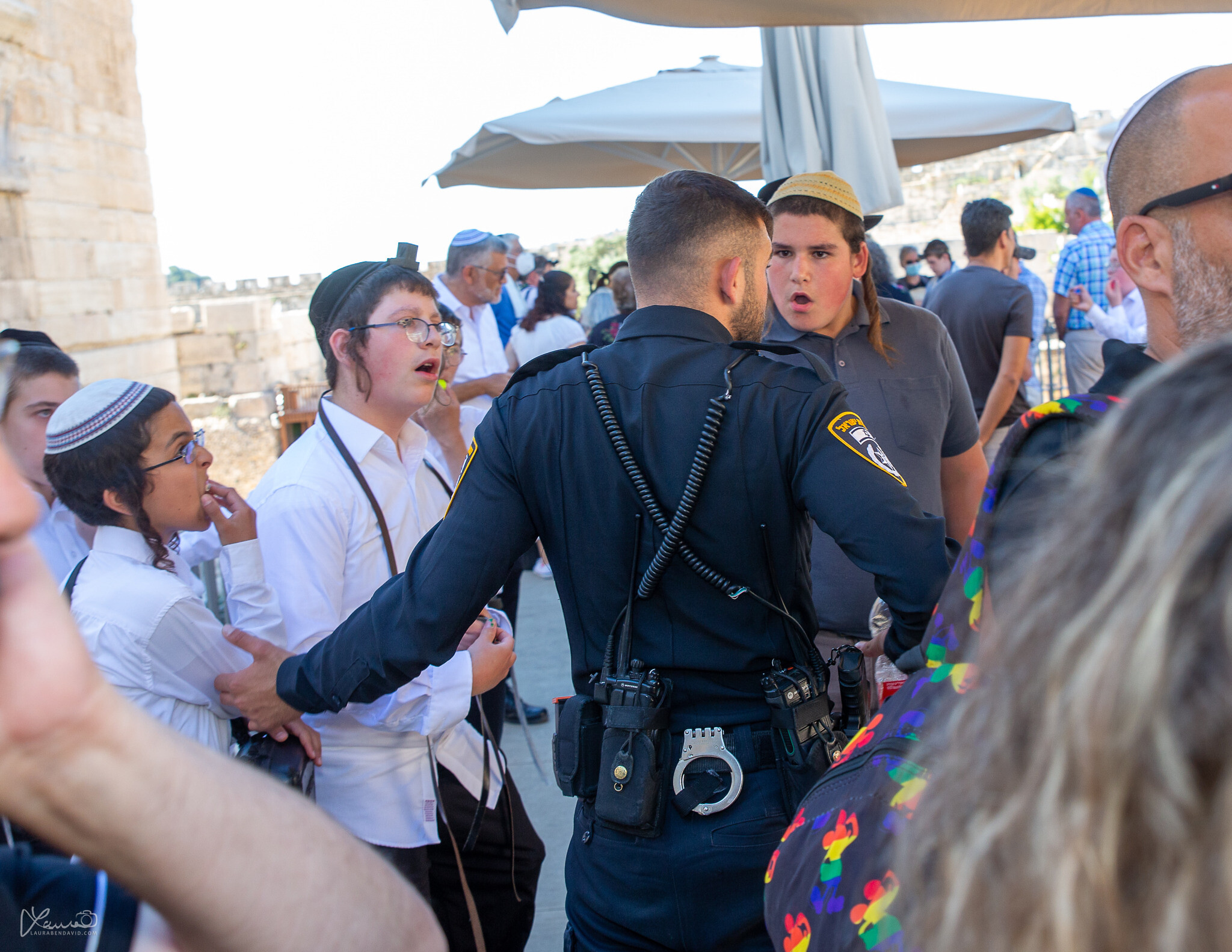 A police officer stands between a group of ultra-Orthodox youths and a bar mitzvah ceremony at the egalitarian section of the Western Wall on June 30, 2022. (Laura Ben-David)