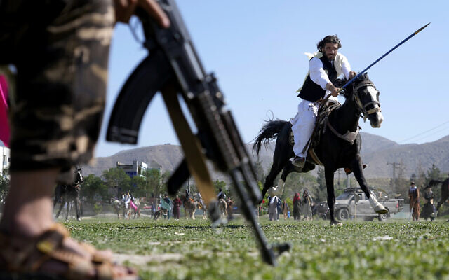 An Afghan man rushes to the target with his horse as a Taliban fighter stands guard during a spear racing in the sprawling Chaman-e-Huzori park in downtown Kabul, Afghanistan, Friday, May 6, 2022. (AP Photo/Ebrahim Noroozi)