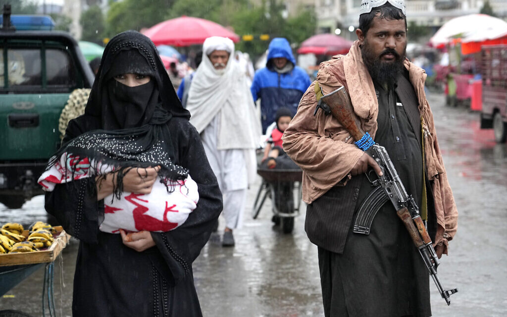 An Afghan woman walks through the old market as a Taliban fighter stands guard, in downtown Kabul, Afghanistan, May 3, 2022.  (AP Photo/Ebrahim Noroozi)