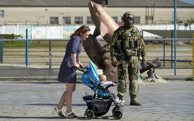 A woman with her child walks past a Russian soldier at an embankment of the Black Sea in Kherson, Kherson region, south Ukraine, May 20, 2022. (AP Photo)