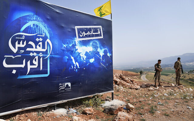 Lebanese army soldiers stand next to a billboard that shows Hezbollah fighters with Arabic that reads: 'Jerusalem is closer, we are coming,' that sits on a hill across from the Israeli town of Metula, on the Lebanese-Israeli border, near the southern Lebanese village of Kfar Kila, Lebanon, Sunday, May 29, 2022. (AP/Hussein Malla)