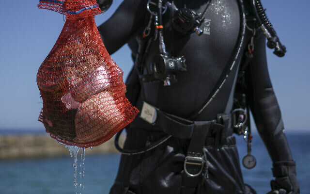 A scuba-diving volunteer shows his collected bag contains trash during World Ocean Day event in the Mediterranean ancient Caesarea's Roman-period port, Israel,  June 10, 2022. (AP Photo/Ariel Schalit)