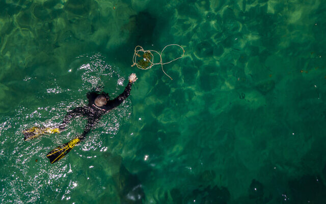 A scuba-diving volunteer collects trash during a World Oceans Day event in the Mediterranean ancient Caesarea's Roman-period port, Israel, June 10, 2022. (AP Photo/Ariel Schalit)