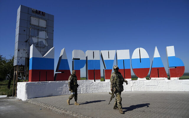Russian soldiers walk past a repainted city name in the colors of the Russian flag at the entrance of Mariupol, on the territory which is under the Government of the Donetsk People's Republic control, eastern Ukraine, June 12, 2022. (AP Photo)