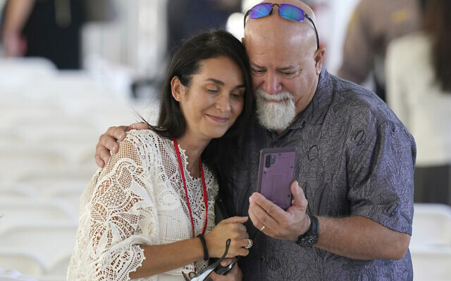 Two attendees gather around a phone before the start of a remembrance event at the site of the Champlain Towers South building collapse, Friday, June 24, 2022, in Surfside, Fla. (AP Photo/Wilfredo Lee)