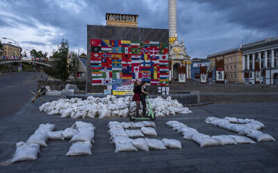 Women ride a scooter through Kyiv's Maidan Square, past sandbags that spell out 'HELP,' and flags displayed from around the world, in Ukraine, June 25, 2022. (Nariman El-Mofty/AP)