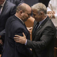Outgoing Prime Minister Naftali Bennett, left, and incoming prime minister Yair Lapid embrace in the Knesset after the passage of a bill to dissolve the parliament and hold new elections, June 30, 2022 (AP Photo/Ariel Schalit)