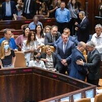 Lawmakers surround Foreign Minister Yair Lapid (left), the incoming interim prime minister, and outgoing premier Naftali Bennett (right) in the Knesset, following a vote to dissolve parliament for new elections, on June 30, 2022. (Olivier Fitoussi/Flash90)