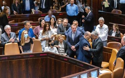 Lawmakers surround Foreign Minister Yair Lapid (left), the incoming interim prime minister, and outgoing premier Naftali Bennett (right) in the Knesset, following a vote to dissolve parliament for new elections, on June 30, 2022. (Olivier Fitoussi/Flash90)