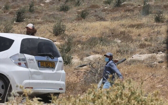 An Israeli settler hurls a stone at left-wing activists near the illegal West Bank outpost of Mitzpe Yair, on June 10, 2022. (Screenshot: Twitter)
