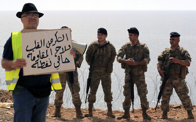 A Lebanese activist holds a placard in Arabic that reads "Thank you from the heart to the weapons of the resistance, protectors of the oil," as Lebanese soldiers stand guard during a protest in the southern border town of Naqoura, Lebanon, Saturday, June 11, 2022. (AP/Mohammed Zaatari)