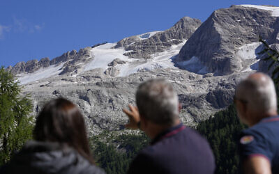 Two Carabinieri officers show to a journalist, left, the Punta Rocca glacier near Canazei, in the Italian Alps in northern Italy, Monday, July 4, 2022, a day after a huge chunk of the glacier broke loose, sending an avalanche of ice, snow, and rocks onto hikers.  (AP Photo/Luca Bruno)