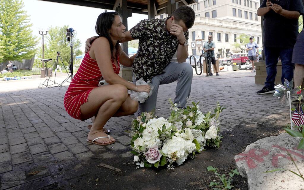 Brooke and Matt Strauss, who were married a day earlier, pause after leaving their wedding bouquets in downtown Highland Park, Ill., near the scene of a mass shooting, on July 5, 2022, in Highland Park, Ill. (AP Photo/Charles Rex Arbogast)