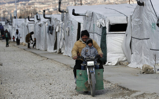 FILE - A displaced Syrian man and his son ride a motorcycle, as they drive between the tents at a refugee camp, in Bar Elias, in eastern Lebanon's Bekaa Valley, March 5, 2021. (AP/Hussein Malla, File)