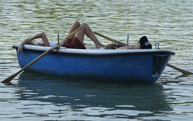 People relax on a pleasure boat on the lake in the Retiro park in Madrid, Spain, July 16, 2022 (AP Photo/Paul White)