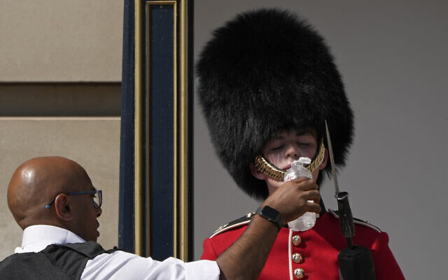A police officer givers water to a British soldier wearing a traditional bearskin hat, on guard duty outside Buckingham Palace, during hot weather in London, July 18, 2022 (AP Photo/Matt Dunham)