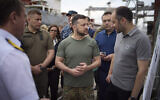 Ukrainian President Volodymyr Zelensky, center, surrounded by ambassadors of different countries and UN officials, visits a port in Chornomork during loading of grain on a Turkish ship, background, close to Odesa, Ukraine, July 29, 2022. (Ukrainian Presidential Press Office via AP)