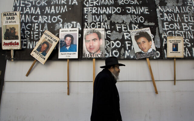 A man walks by a mural covered with names and photographs of the victims of the 1994 bombing of the AMIA Jewish community center on the 19th anniversary of the terror attack in Buenos Aires, Argentina, Thursday, July 18, 2013. (AP/Victor R. Caivano)
