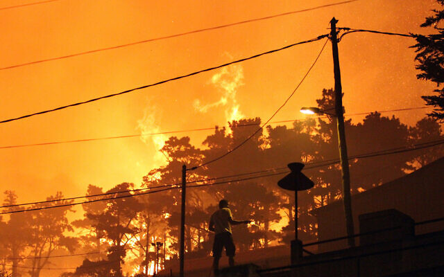 Illustrative: A man uses a garden hose to spray water on the roof of houses as forest fires rage nearby on the hills above the city of Funchal in the Portuguese Atlantic island of Madeira, July 18 2012. (AP/Joana Sousa)