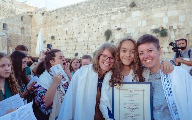 Lucia da Silva, 12, from Seattle, Washington, surrounded by her mothers Cara Stoddard (right) and Ada Danelo in front of the Western Wall, July 29, 2022 (Tal Kfir Shor via JTA)