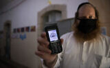 A man holds up  his cellular phone certificating that it is 'kosher' at the entrance to an ultra-Orthodox school in Jerusalem on May 6, 2020. (Nati Shohat/ Flash90)