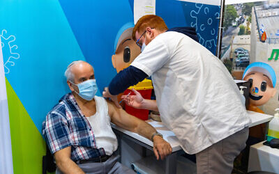 An elderly Israeli man receives a dose of the COVID-19 vaccine, at vaccination center soon after fourth shots were introduced. (Olivier Fitoussi/Flash90)