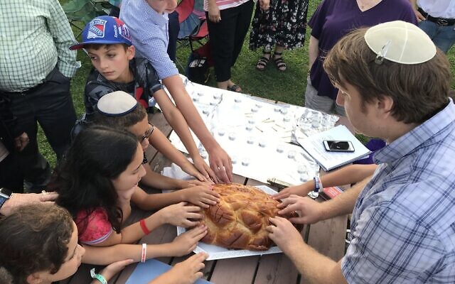 Rabbi Matt Abelson, right, makes the blessing over bread with children of the Jericho Jewish Center at Shabbat in the park, 2019. (Leslie Hartman)