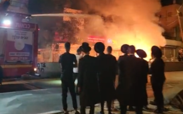 Illustrative: A group of Haredi men watch as a firetruck works to extinguish a fire caused by riots at the Bar Ilan Junction in Jerusalem, July 7, 2022. (Screenshot/Twitter)
