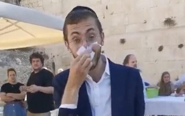 An ultra-Orthodox youth wipes his nose with a page torn from a siddur at the egalitarian section of the Western Wall on June 30, 2022. (Screen capture: Masorti movement on Twitter)