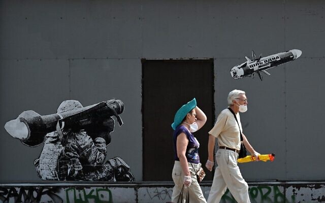 A couple walks past a graffiti on a wall depicting a Ukrainian serviceman making a shot with a US-made Javelin portable anti-tank missile system, in Kyiv, on July 29, 2022. (Sergei SUPINSKY / AFP)