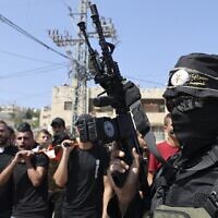 A gunman affiliated with the Palestinian Islamic Jihad terror group, marches as men carry the body of Dirar al-Kafrayni, killed during clashes with Israeli troops in the West Bank city of Jenin, during his funeral at the Jenin refugee camp, on August 2, 2022. (Jaafar Ashitiyeh/AFP)