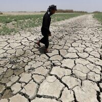 A man walks on cracked and dried up soil in the Hawiza marsh near the city of al-Amarah in southern Iraq on July 27, 2022. (AHMAD AL-RUBAYE / AFP)